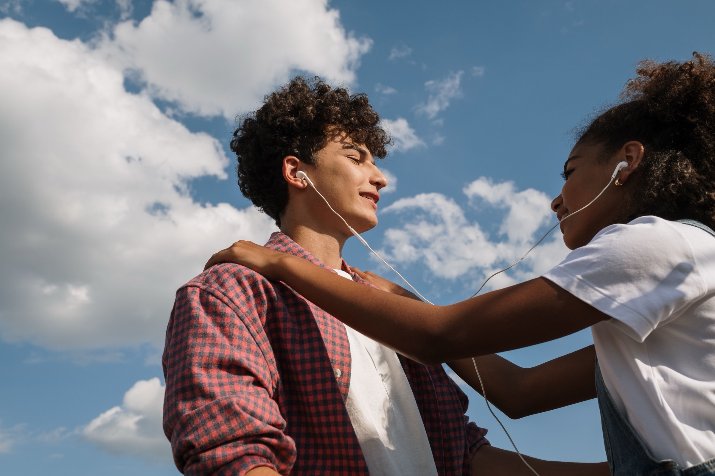 A kept photo — two friends sharing earbuds under a blue summer sky